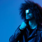 Portrait of fashion man with curly hair with stylish glasses on blue background multinational