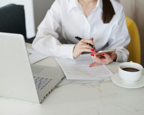 Workspace shot from above with woman working on laptop and signing contract and with coffee cup