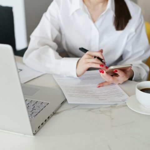 Workspace shot from above with woman working on laptop and signing contract and with coffee cup