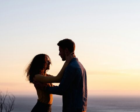 man and woman standing near body of water during sunset