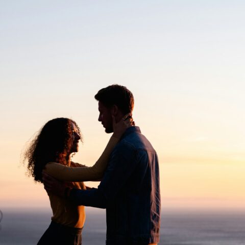 man and woman standing near body of water during sunset