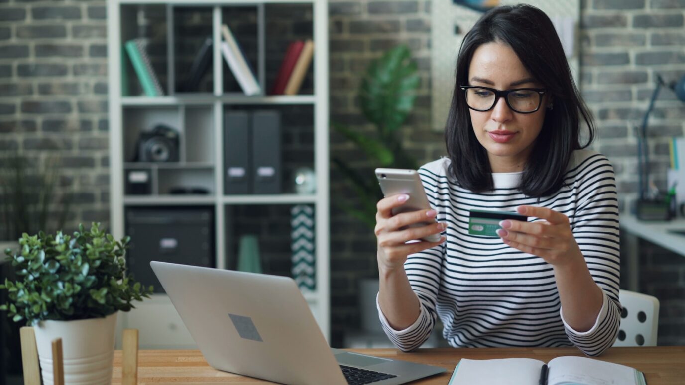 a woman sitting at a table looking at her cell phone, discount calculate