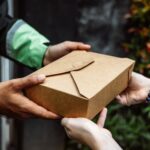 Close-up of a delivery person handing over a box to a customer outdoors.