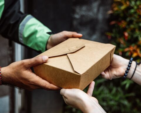 Close-up of a delivery person handing over a box to a customer outdoors.