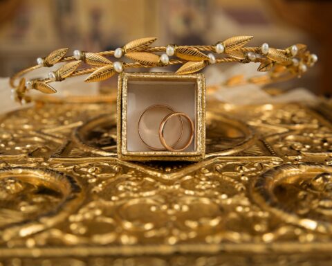 Close-up of gold wedding rings and a delicate tiara on an ornate golden background, symbolizing luxury and elegance.