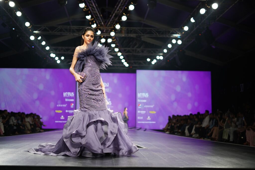 A model in a stunning purple gown walks the runway at a prestigious fashion event.
