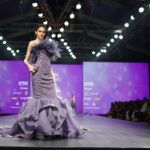 A model in a stunning purple gown walks the runway at a prestigious fashion event.