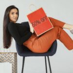 Stylish woman in chic pose holding a 50% off shopping bag, surrounded by bags.