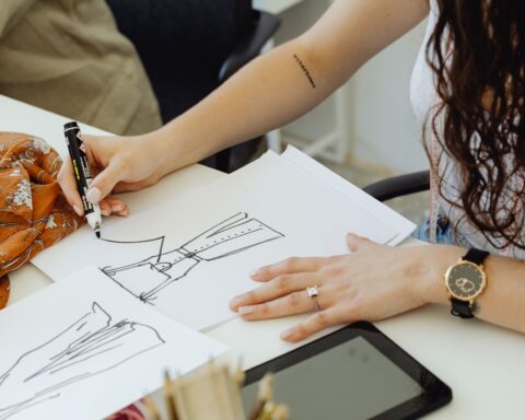 Fashion designer sketching dress ideas at a desk with fabric and sketches.