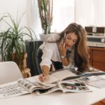 Businesswoman multitasking at desk with magazines, writing notes and talking on phone.