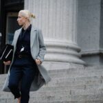 Serious female lawyer in elegant outfit holding folders with documents while going downstairs near stone state building and looking away