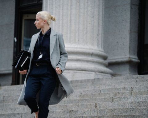 Serious female lawyer in elegant outfit holding folders with documents while going downstairs near stone state building and looking away