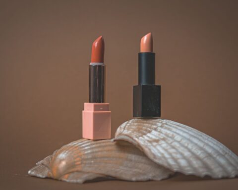 Two elegant lipsticks displayed on a seashell with a minimalist, earthy backdrop.