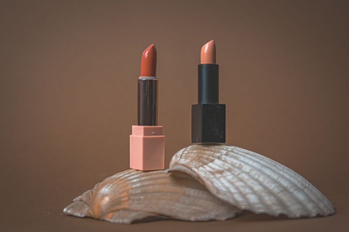 Two elegant lipsticks displayed on a seashell with a minimalist, earthy backdrop.