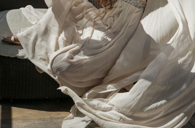 Portrait of a woman in a flowing white dress, exuding elegance and grace outdoors.