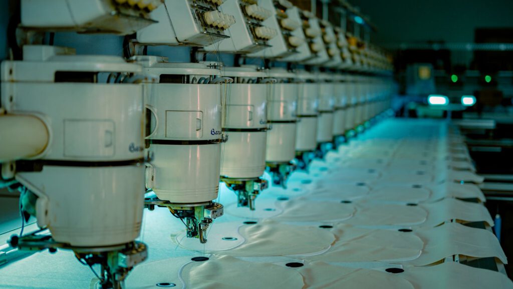 Row of industrial sewing machines in a garment factory, where a tech pack is used to make clothing