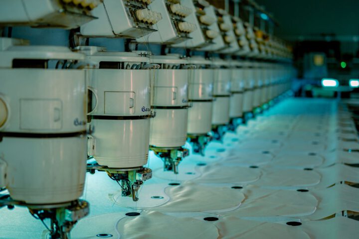 Row of industrial sewing machines in a garment factory, where a tech pack is used to make clothing
