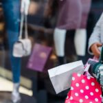Crop anonymous women friends in stylish clothes standing with shopping bags near counter of boutique in daytime