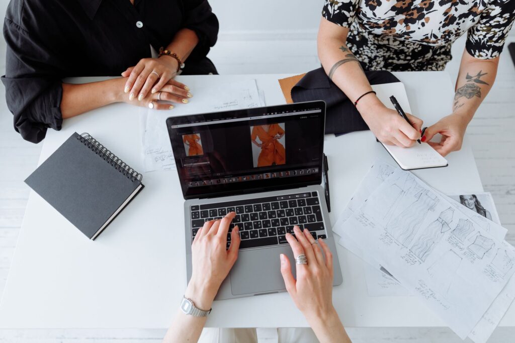 Three people working together on a laptop, reviewing fashion designs at a table.