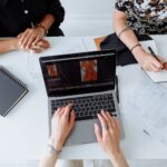 Three people working together on a laptop, reviewing fashion designs at a table.