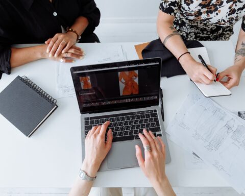 Three people working together on a laptop, reviewing fashion designs at a table.