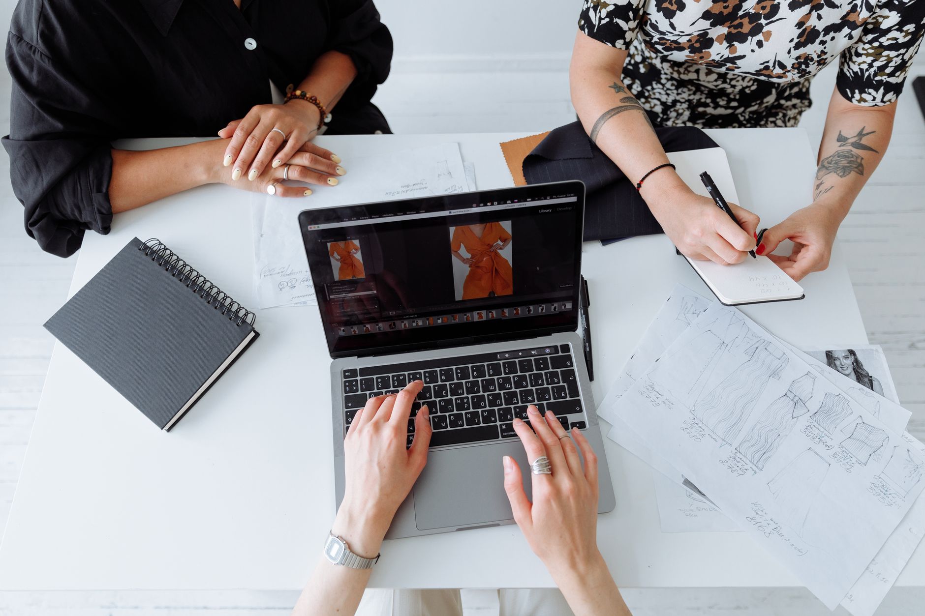 Three people working together on a laptop, reviewing fashion designs at a table.