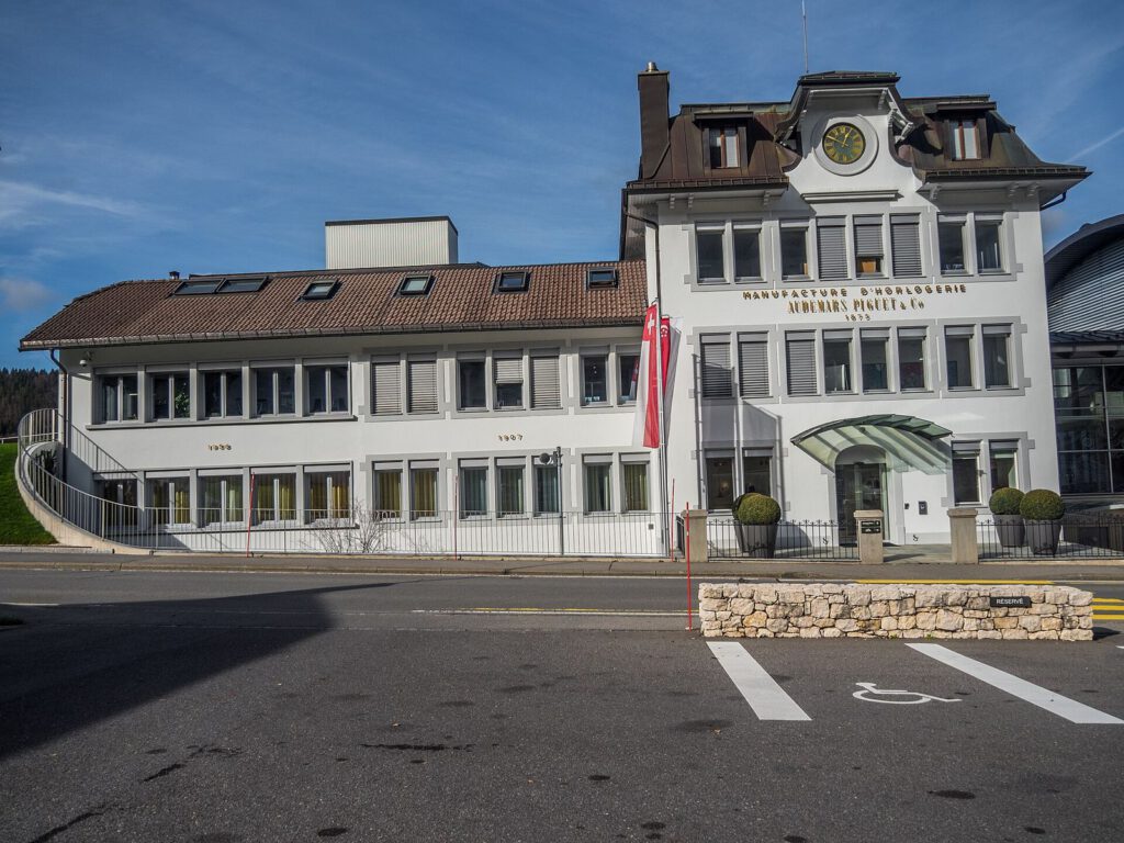 Audemars Piguet's historic manufacture building in Le Brassus with a clock and the company name on its white facade