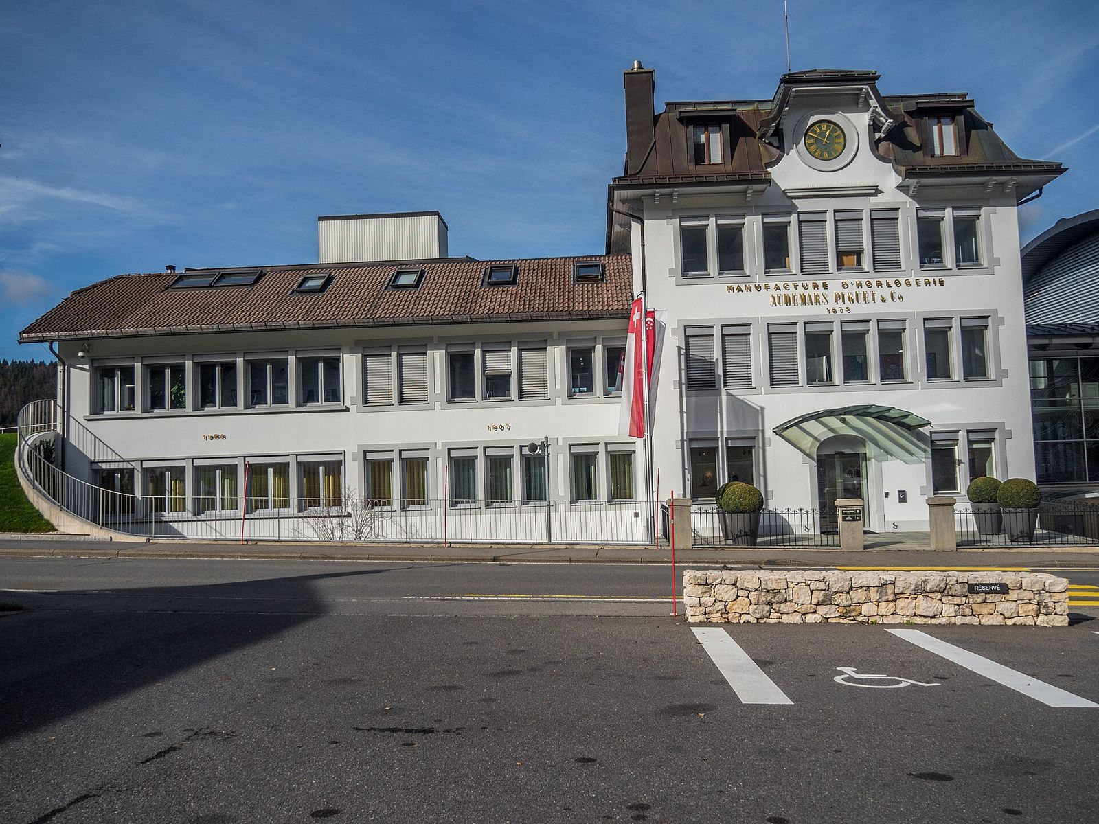 Audemars Piguet's historic manufacture building in Le Brassus with a clock and the company name on its white facade