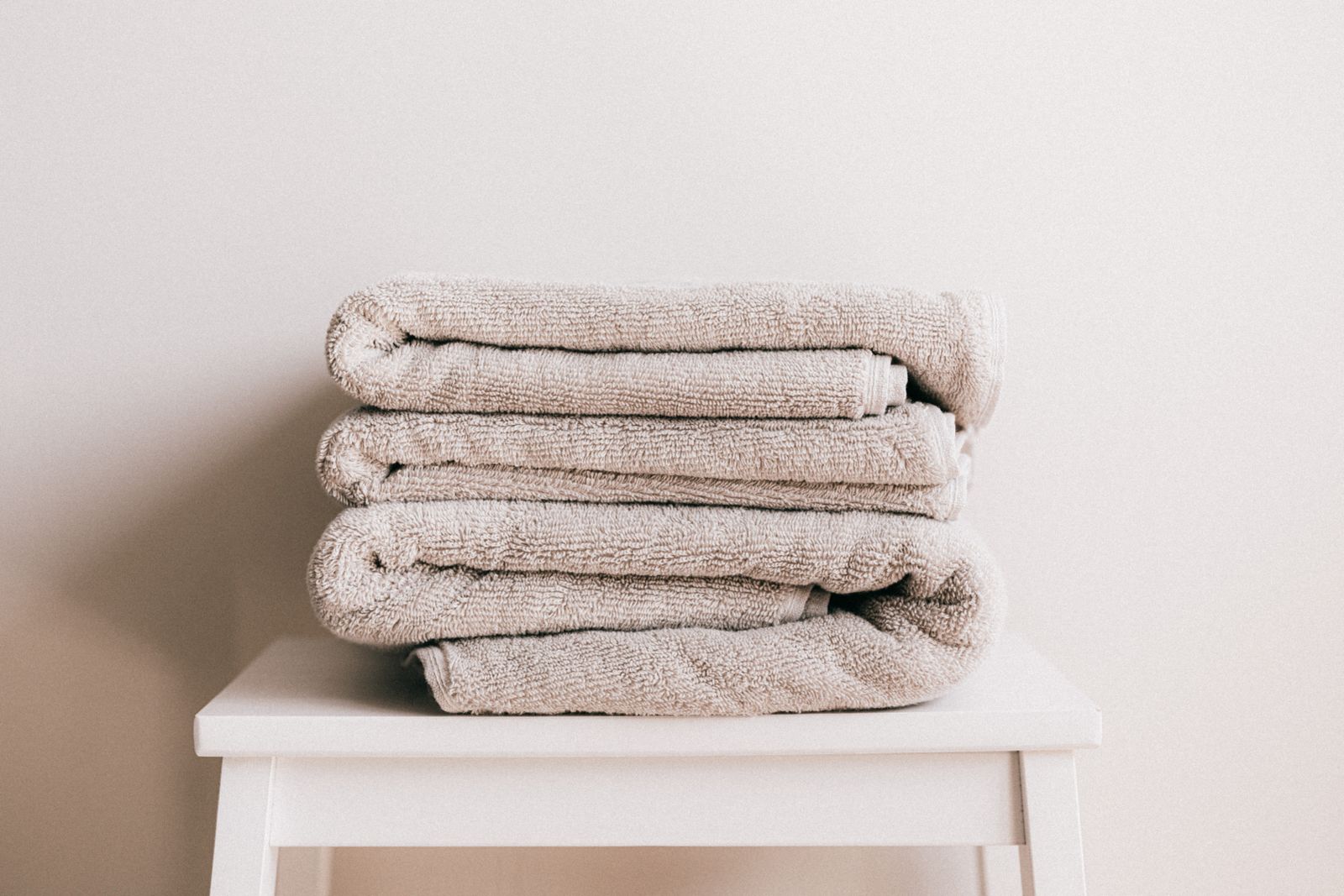 Stack of soft beige folded towels on a white stool against a plain wall