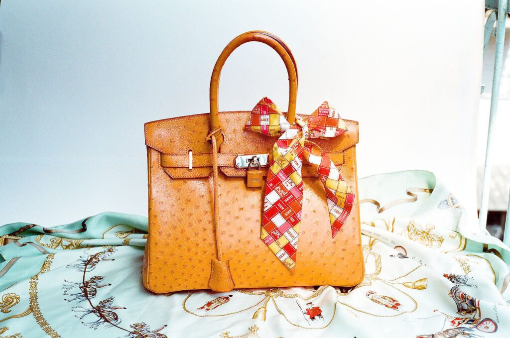 Tan ostrich leather Hermès Birkin 30 with a twilly on a silk scarf, illustrating Birkin bag price