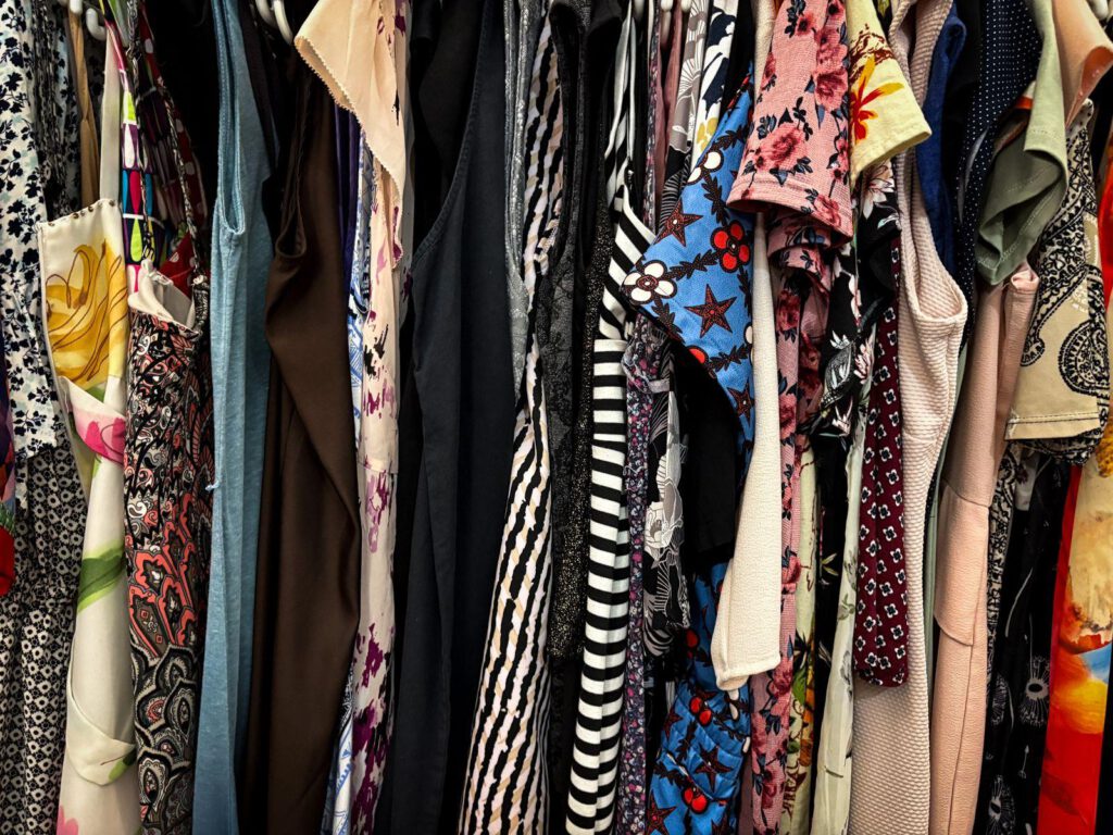 Rack of colourful second-hand dresses and tops hanging close together in a thrift shop