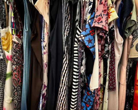 Rack of colourful second-hand dresses and tops hanging close together in a thrift shop