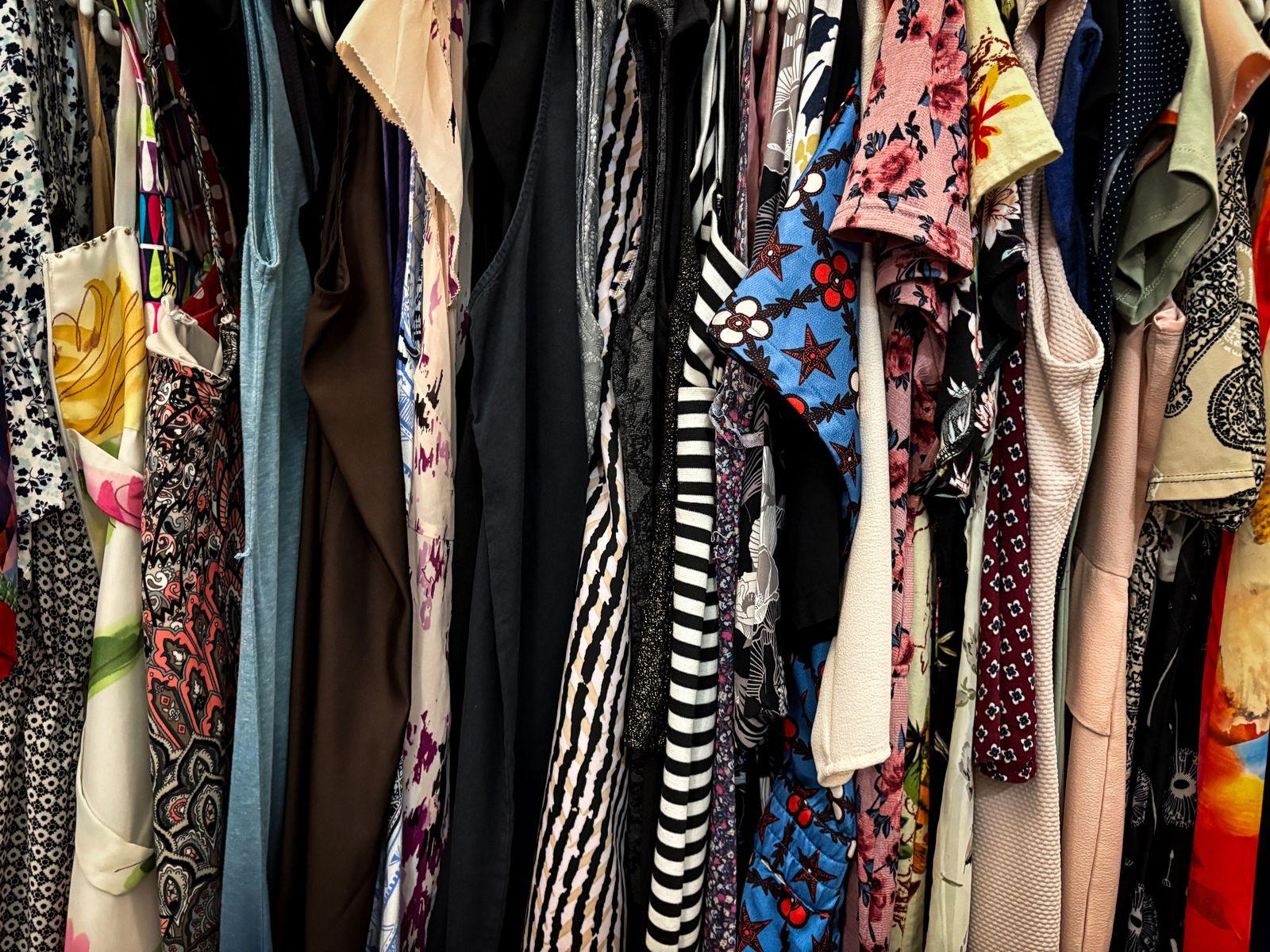 Rack of colourful second-hand dresses and tops hanging close together in a thrift shop