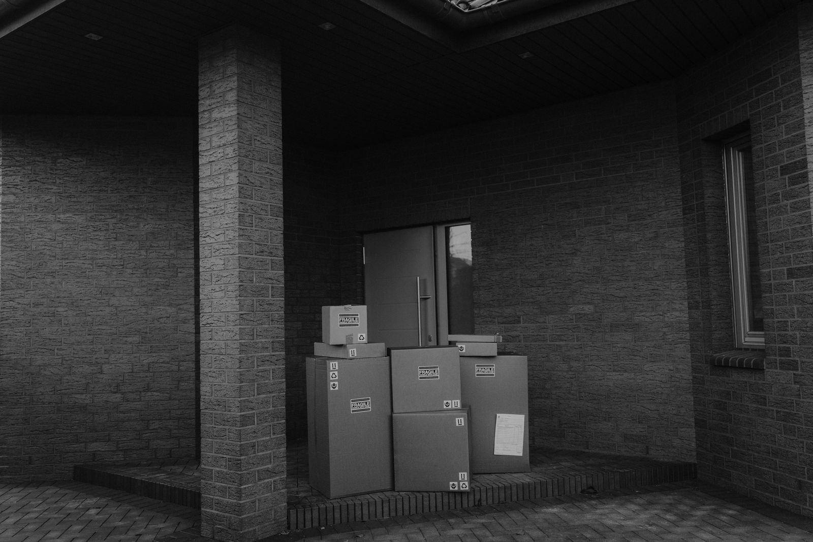 Black and white photo of cardboard parcels stacked at a building doorway, representing online marketplace orders