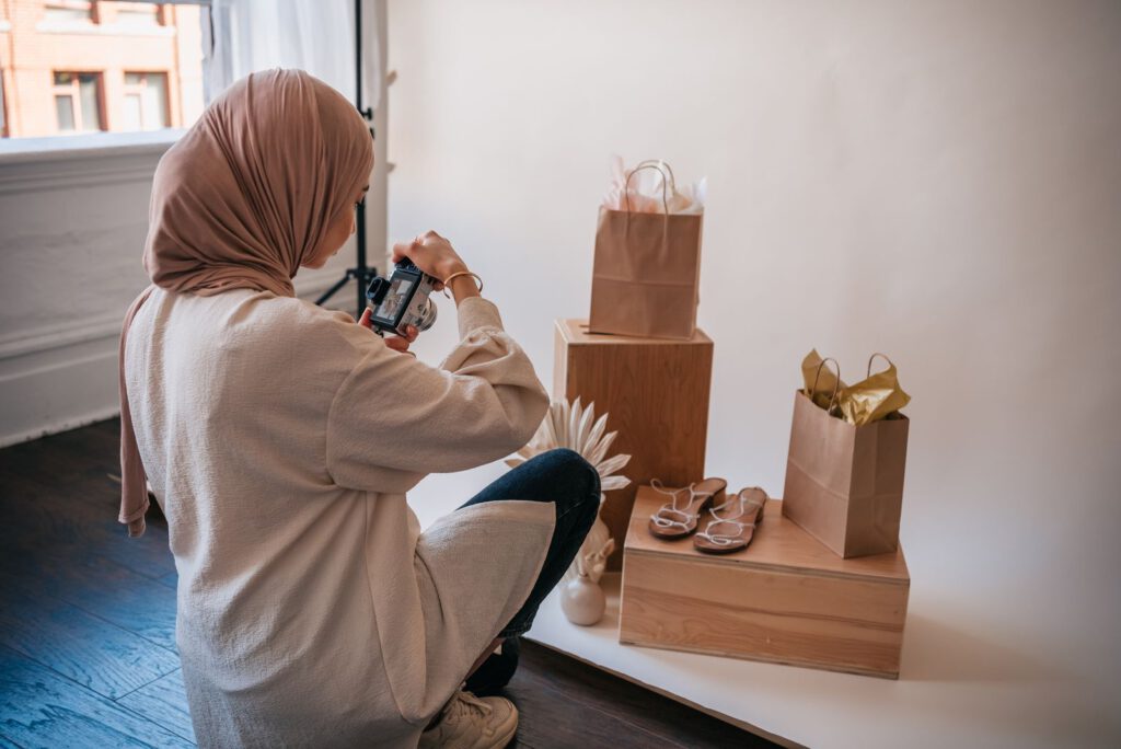 Woman photographing sandals and paper shopping bags on wooden boxes during a product photo shoot