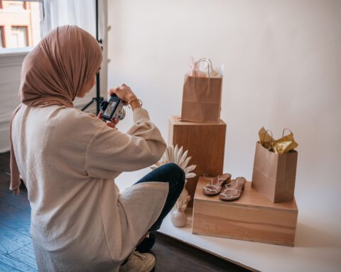 Woman photographing sandals and paper shopping bags on wooden boxes during a product photo shoot