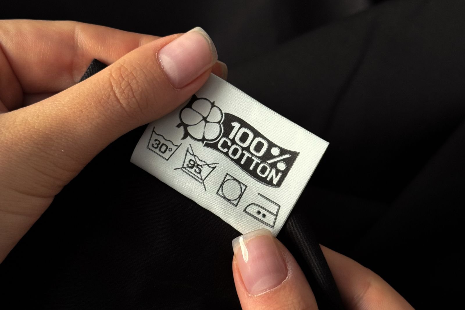 Hands holding a garment care label reading 100% cotton with washing symbols