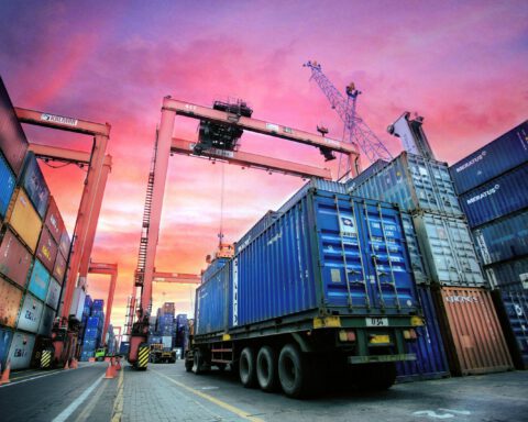 Shipping containers stacked at a busy port at sunset