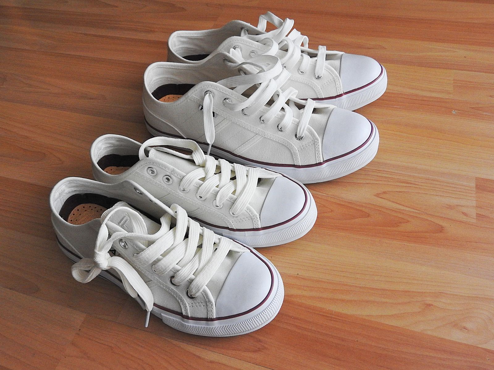 Two pairs of plain white low-top canvas sneakers on a wooden floor, a generic style no brand can own