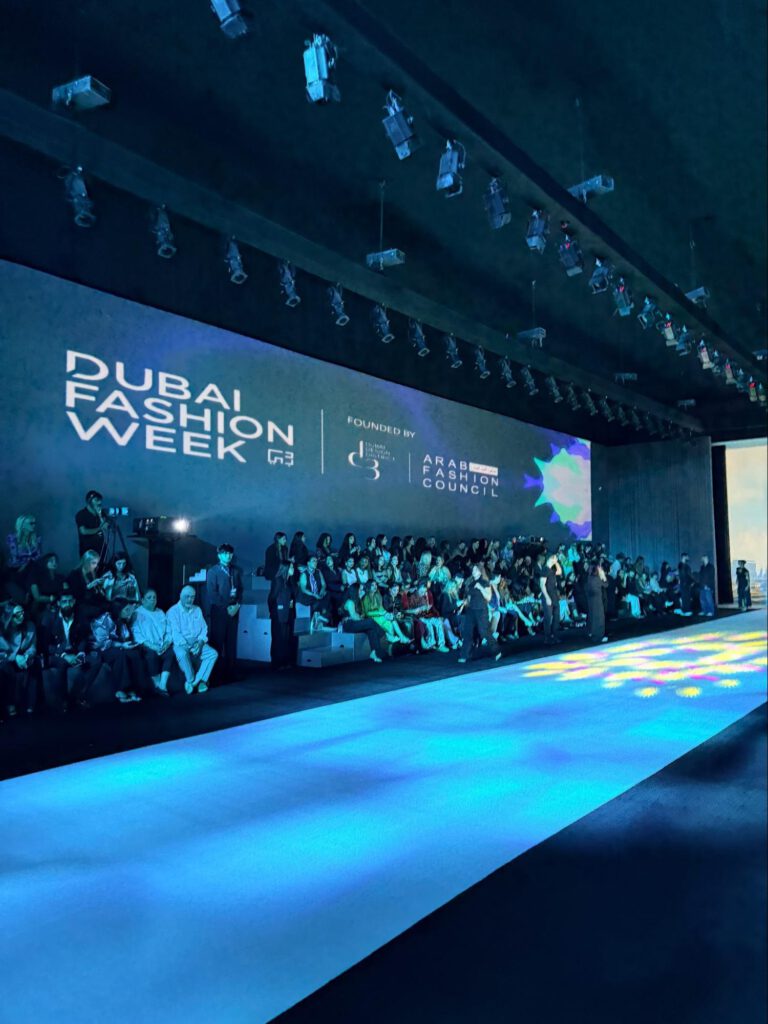 The Dubai Fashion Week runway and seating at Dubai Design District, with the event backdrop lit in blue