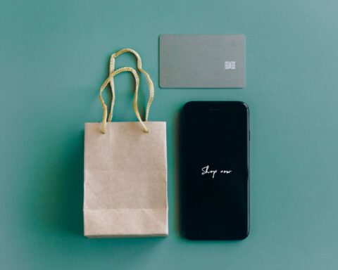 Smartphone showing Shop now beside a plain bank card and small paper bag, illustrating buying from DHgate online