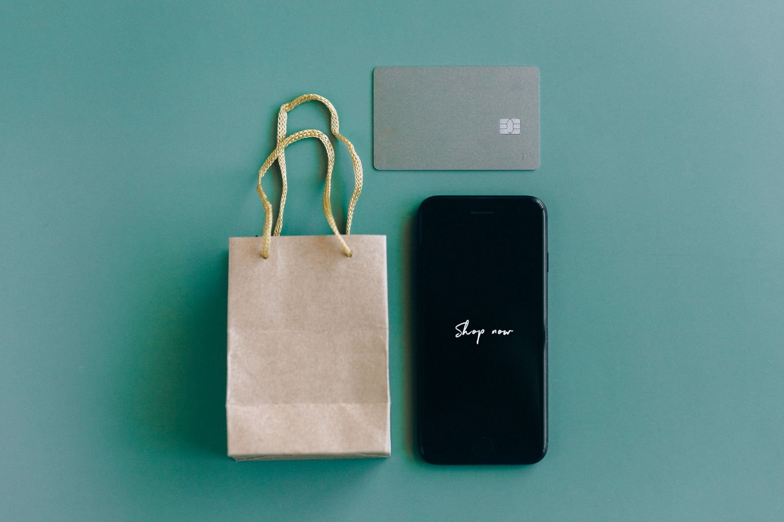 Smartphone showing Shop now beside a plain bank card and small paper bag, illustrating buying from DHgate online