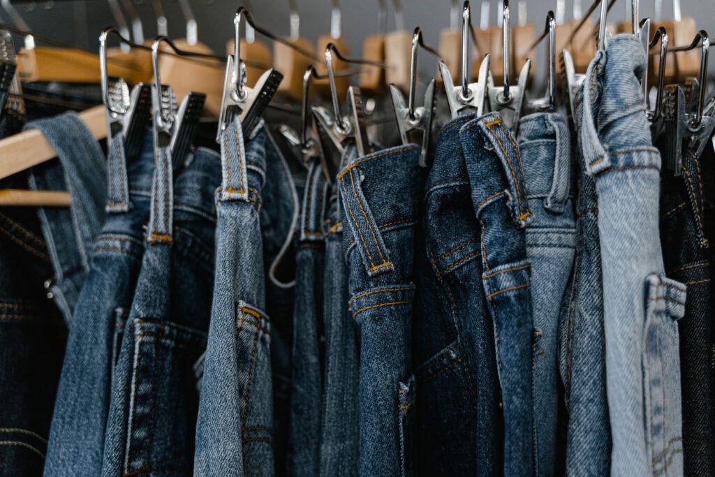 Row of blue denim jeans hanging from clip hangers on a clothing rail, representing PVH's jeanswear brands