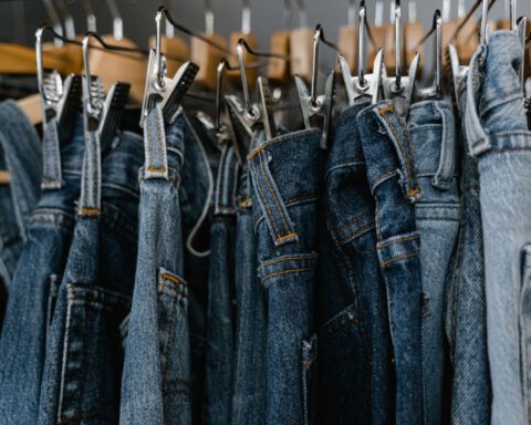 Row of blue denim jeans hanging from clip hangers on a clothing rail, representing PVH's jeanswear brands