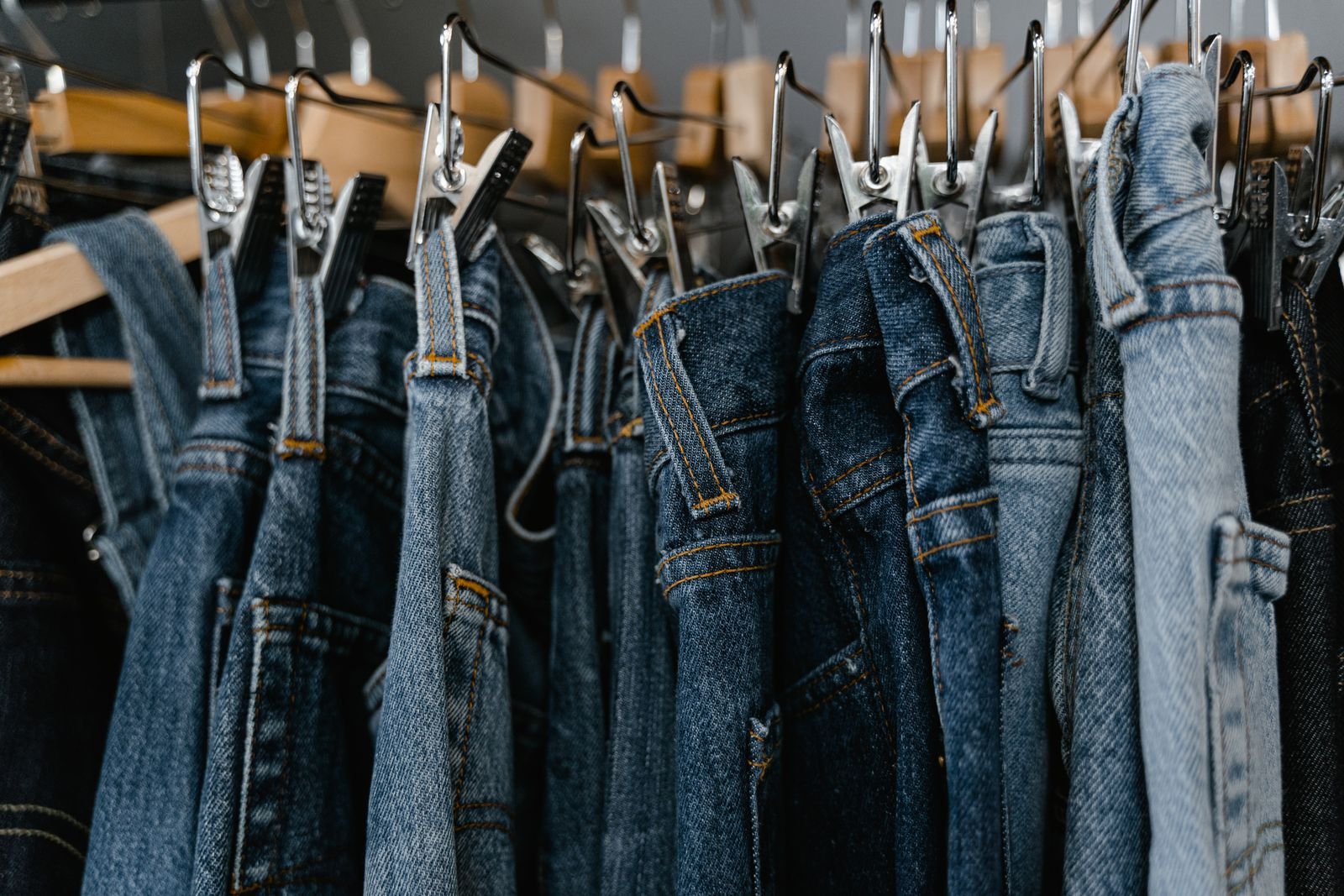 Row of blue denim jeans hanging from clip hangers on a clothing rail, representing PVH's jeanswear brands