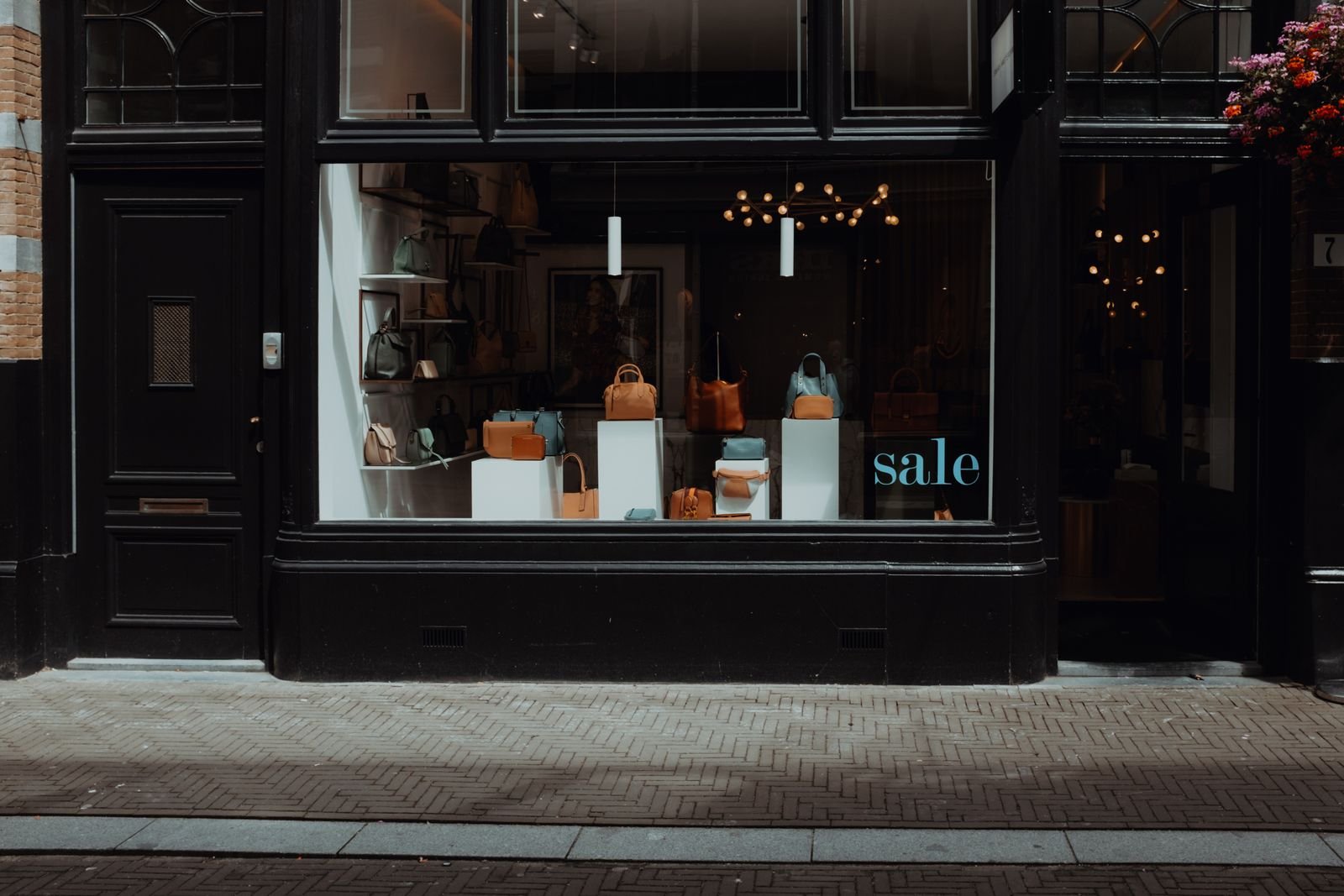 Dark shopfront with leather handbags on white plinths in the window and a sale sign on the glass