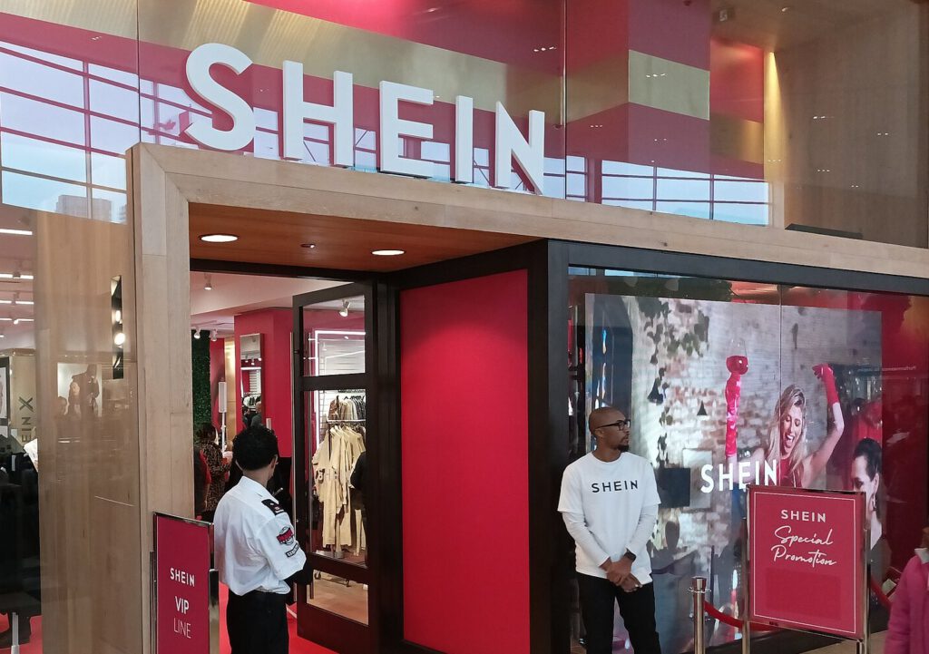 Shein pop-up store entrance with a large white Shein sign, red walls, a VIP line sign and staff at the door