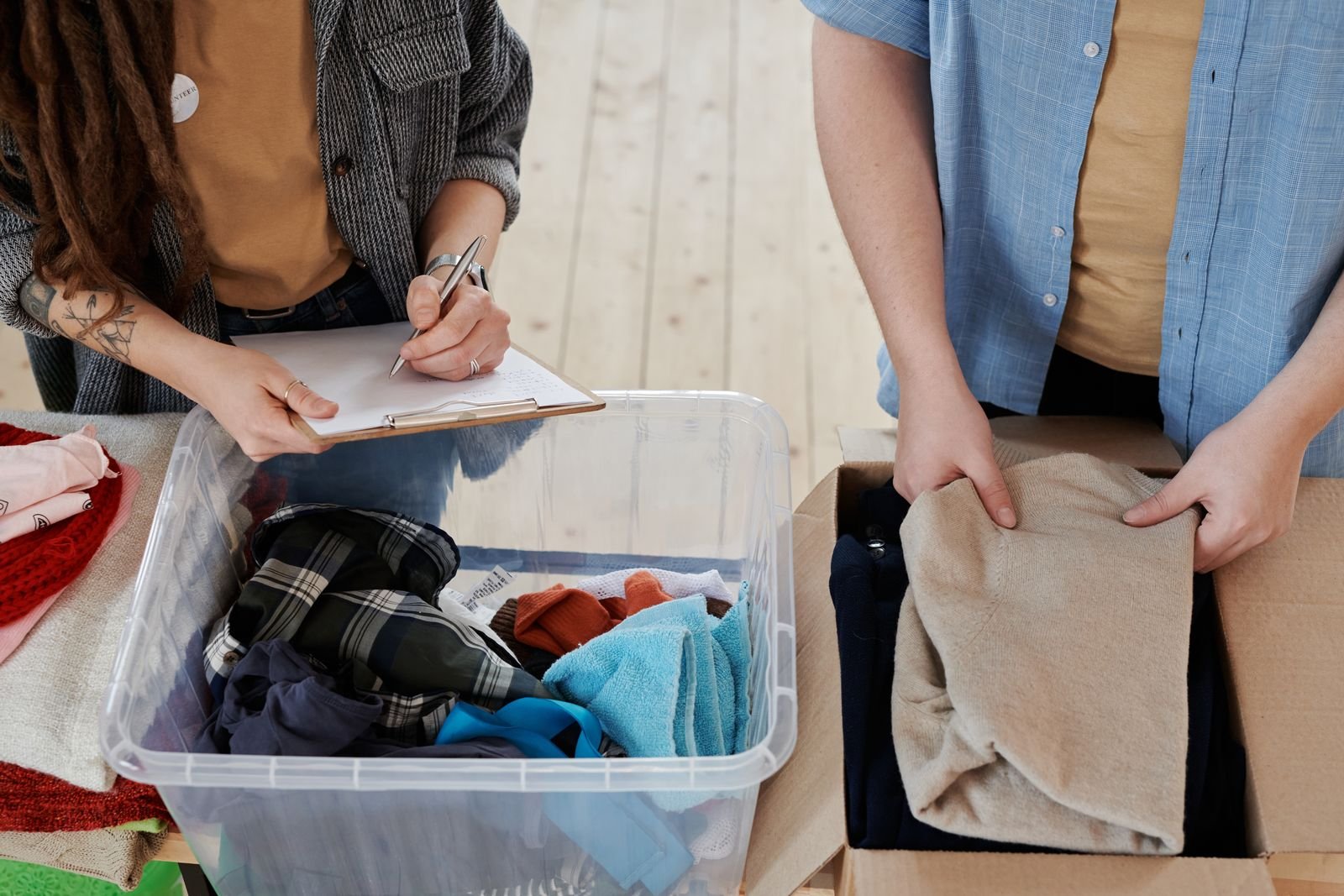Two volunteers sorting used clothes into a plastic tub and cardboard box while one records items on a clipboard