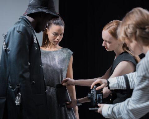 Two models in a studio while a stylist adjusts an outfit and a photographer checks the camera
