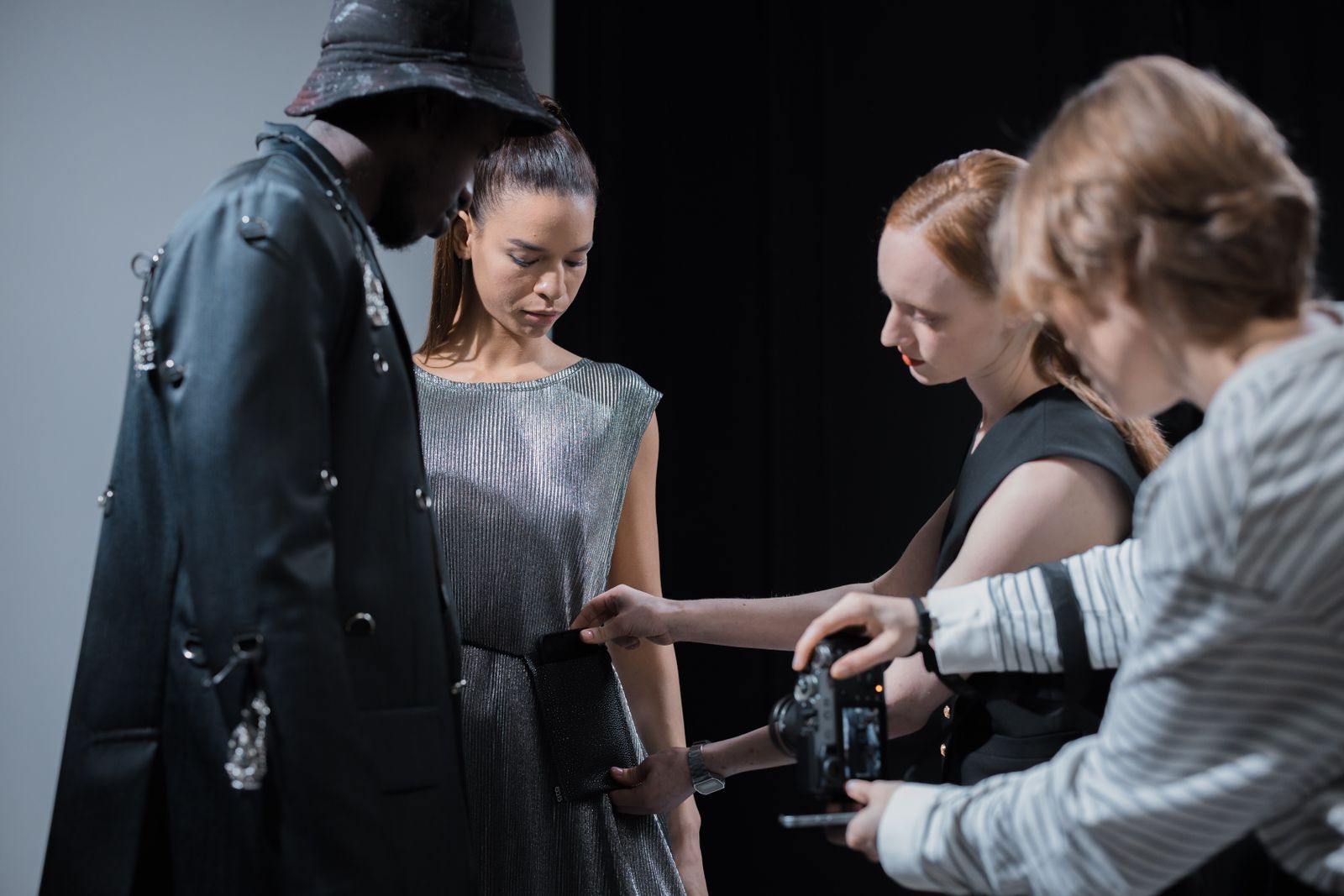 Two models in a studio while a stylist adjusts an outfit and a photographer checks the camera